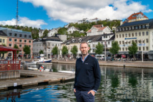 Mann står ved brygga i Arendal sentrum med båter, bygninger og sjø i bakgrunnen.